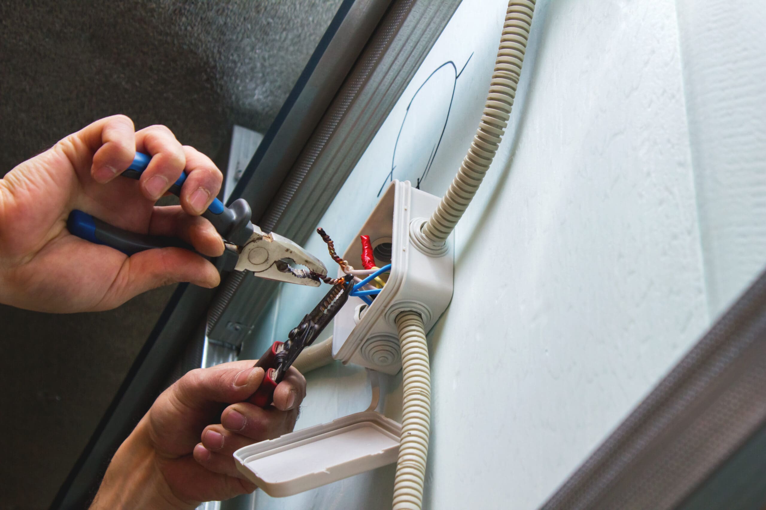 Close-up of a person using pliers to work on electrical wiring inside a wall-mounted junction box.